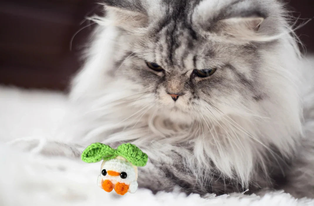 Fluffy long-haired cat focused on small woven Chunkle & Puff chick cat toy with green leaf top, soft textured design for batting and pouncing, botanical infused independent play cat toy