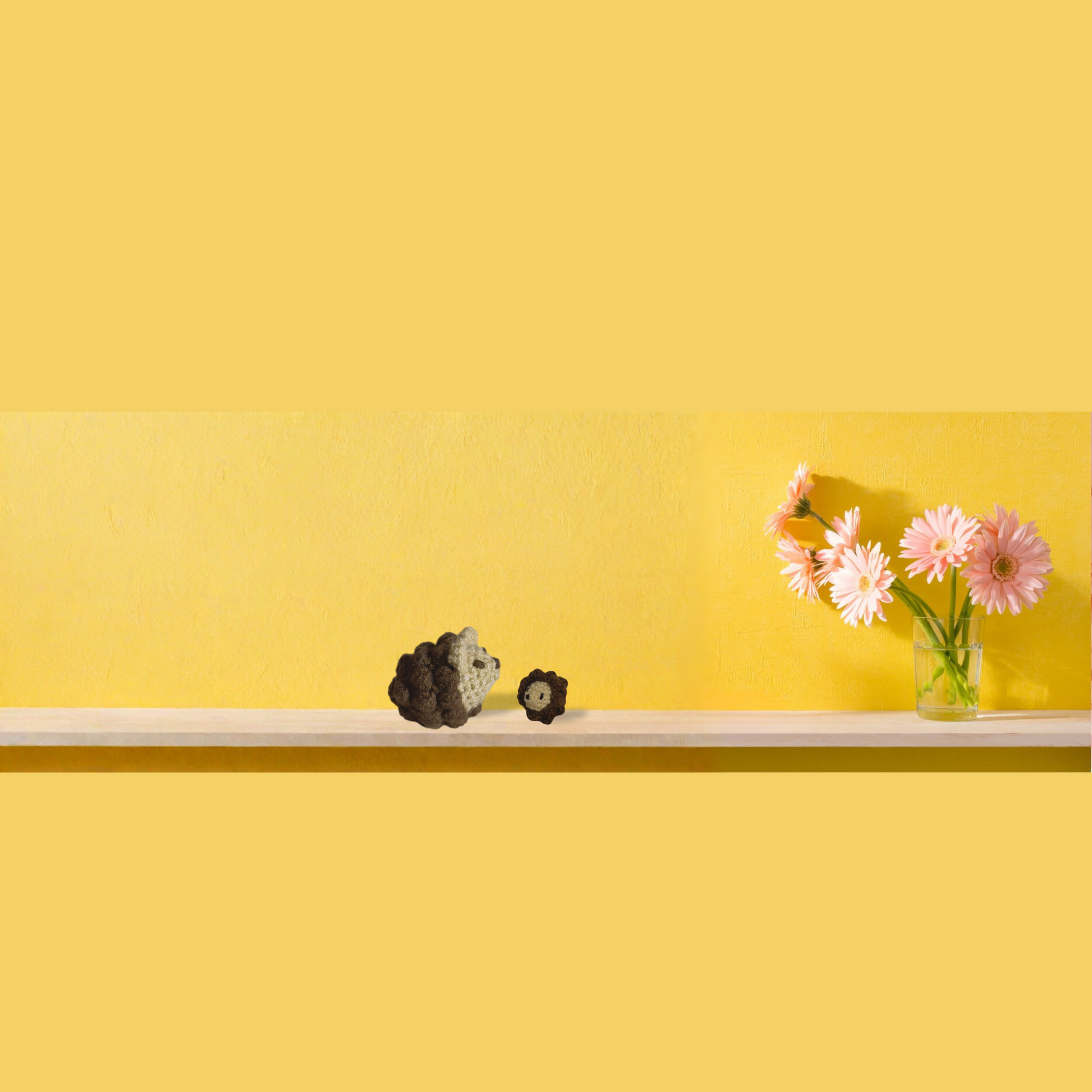 Two woven Chunkle & Puff cat toys displayed on shelf against yellow wall beside pink flowers in glass vase, textured artisan cat toys designed for batting and carrying, botanical infused independent play cat toys