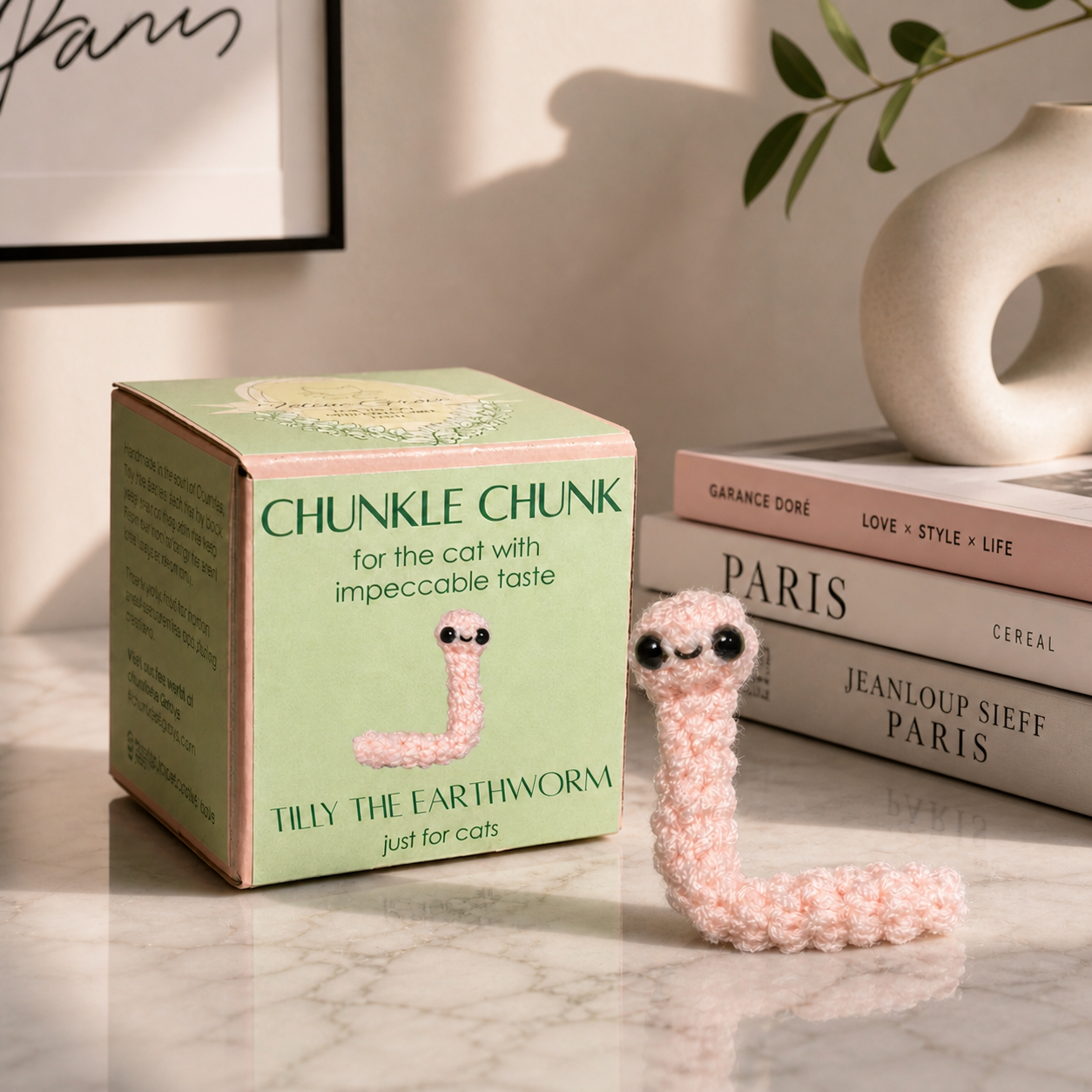 Blush pink woven earthworm cat toy beside green Chunkle & Puff box labeled Tilly the Earthworm, luxury cat toy packaging from Feline Grove infused with Miracle Nip botanical blend