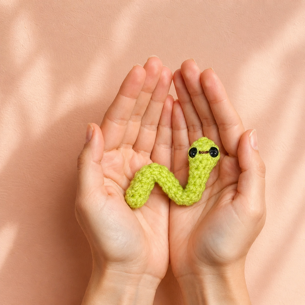 Artisan woven green inchworm cat toy resting in cupped hands, soft textured surface and palm-sized scale, lightweight curved shape for batting and carrying, Chunkle & Puff toy infused with Miracle Nip botanical blend