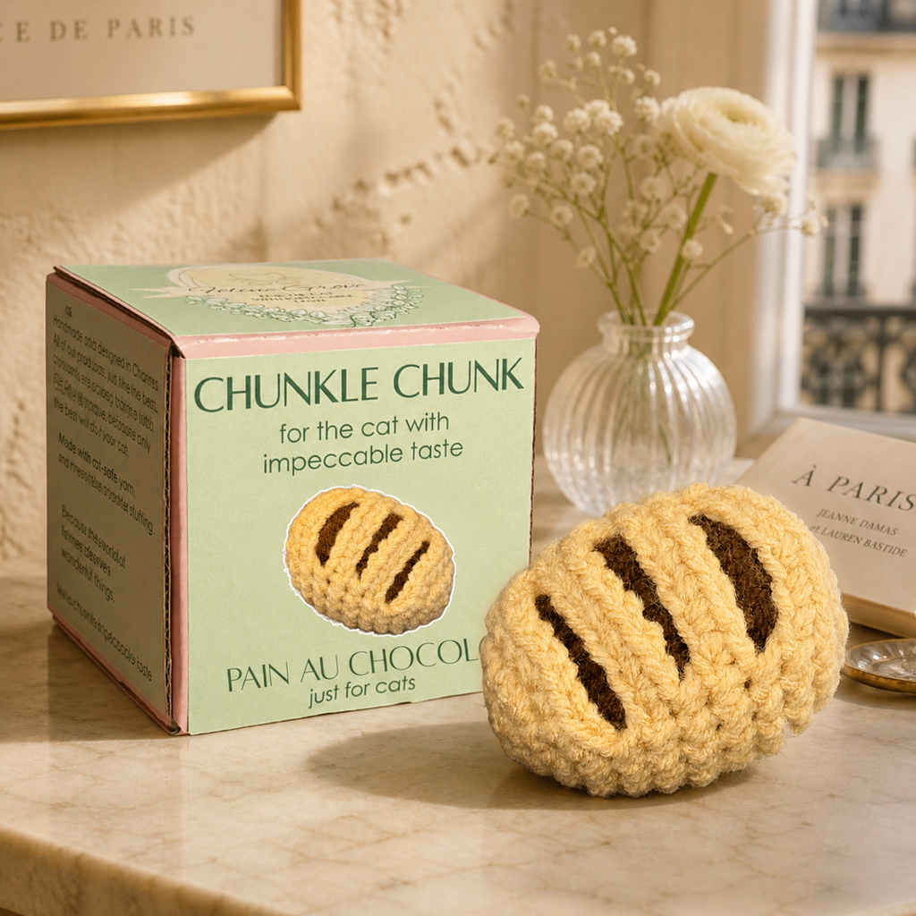 French cat toy. Chocolate croissant shaped Chunkle Puff with Feline Grove gift box on olive green background, woven botanical cat toy from the France collection