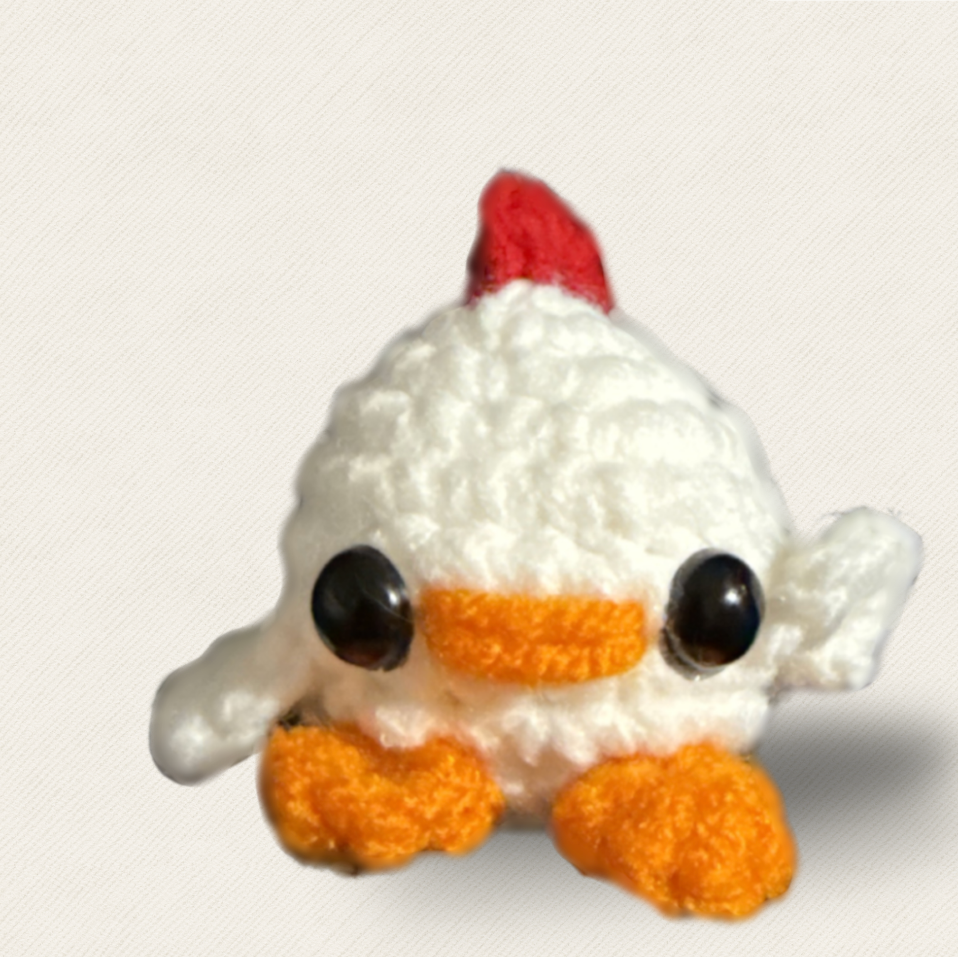 Cat Toy Chick Weighted. Close front view of a tiny white woven chick cat toy with rounded body, plush yarn texture, glossy black eyes, orange beak and feet, and a red comb against a light fabric background.