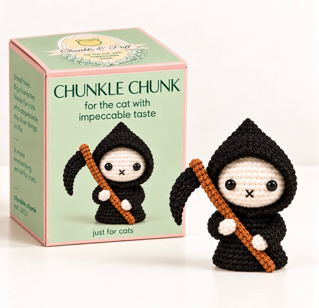 cat toy for halloween. A crocheted amigurumi grim reaper character toy stands beside its branded retail box. The toy is dressed in black with a cream face and hands, holding an orange scythe.