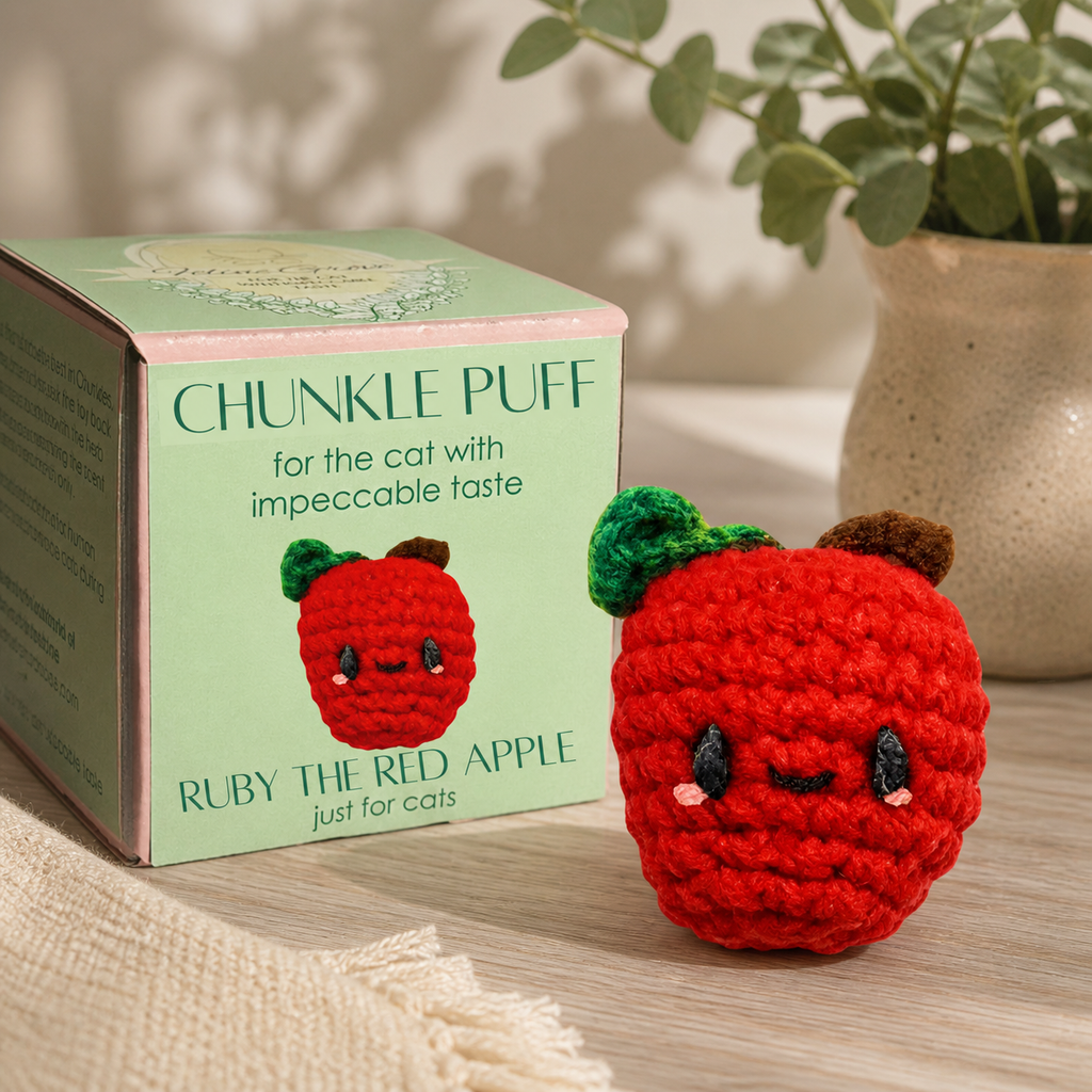 Red woven apple cat toy beside a mint green Chunkle Puff box on a warm tabletop with soft plant shadows and cozy boutique styling.