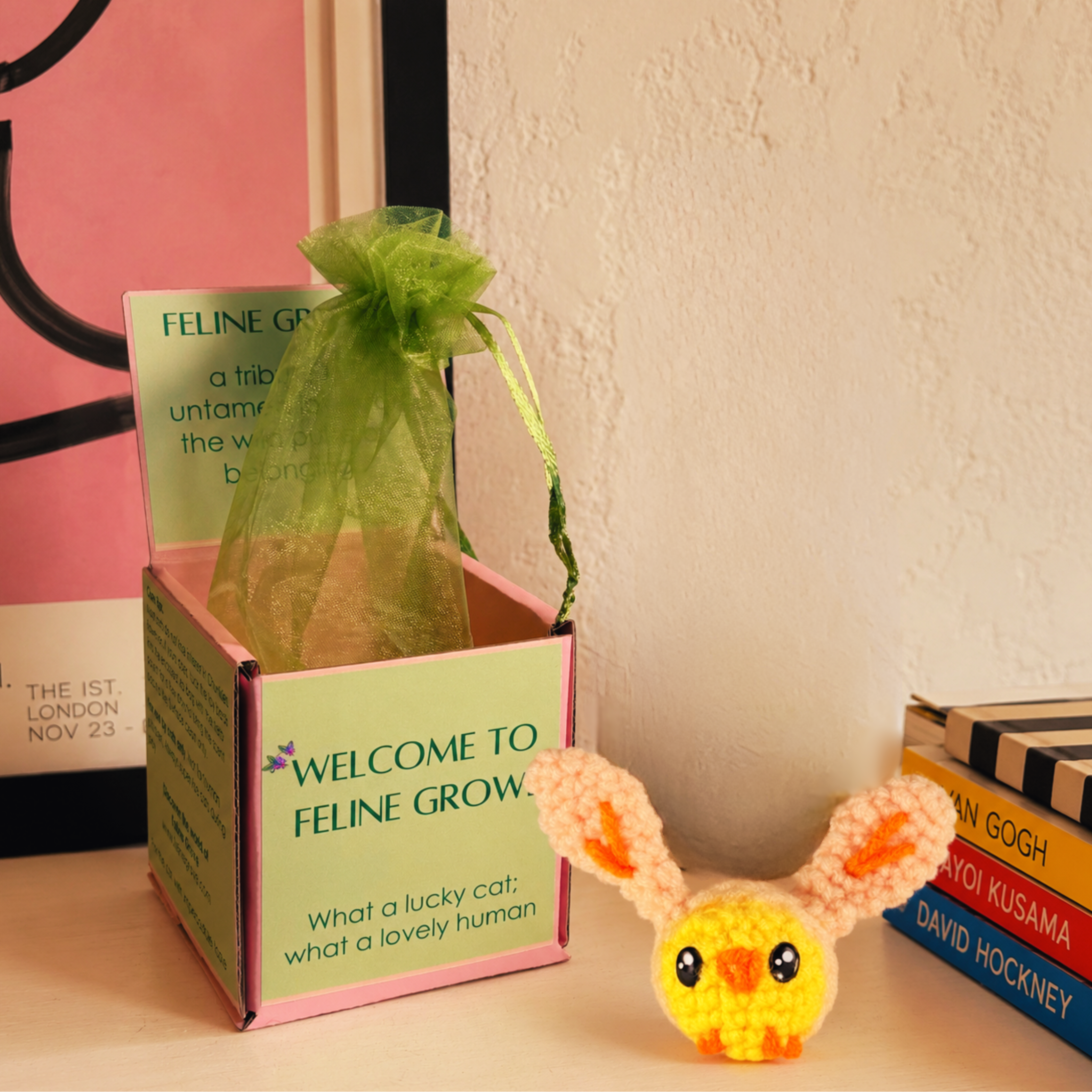Cat toy chick in rabbit costume. Wally the Chick artisan cat toy in soft yellow and cream yarn with long ears, displayed beside Feline Grove gift box and green organza pouch; small, plush, hand-woven texture shown in packaging presentation.