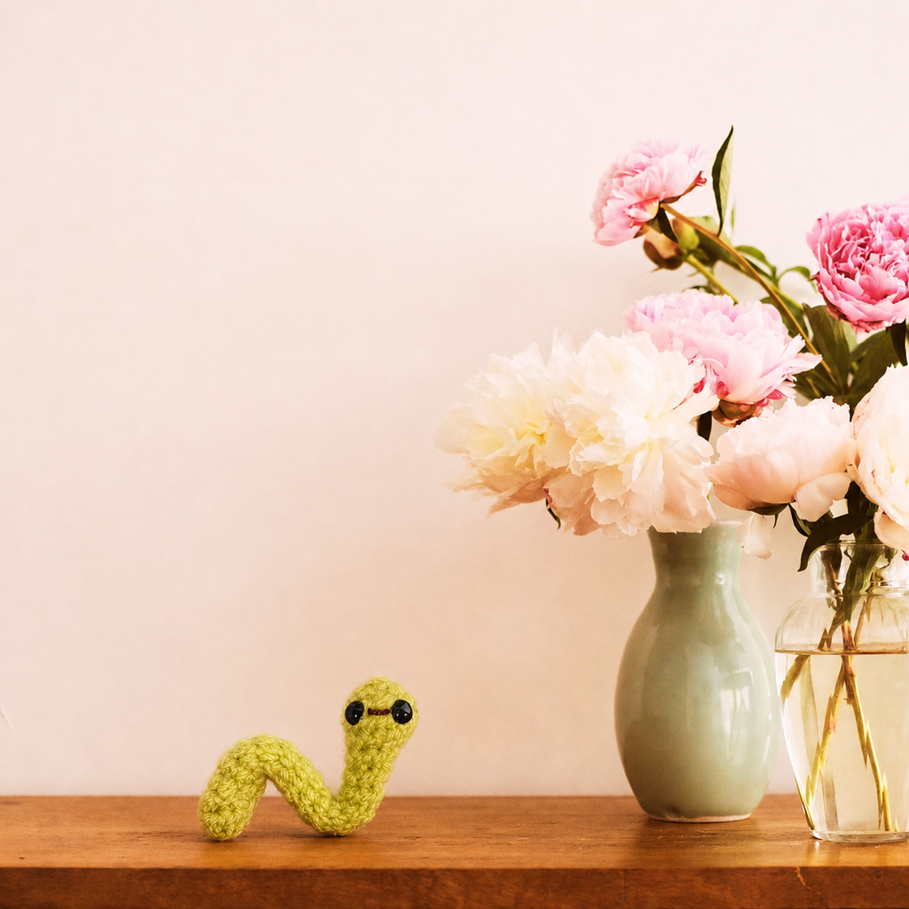 Bright green woven inchworm cat toy on wooden table beside pastel vases and flowers, soft textured surface and small curved form, designed for independent play, Chunkle & Puff toy with Miracle Nip botanical blend