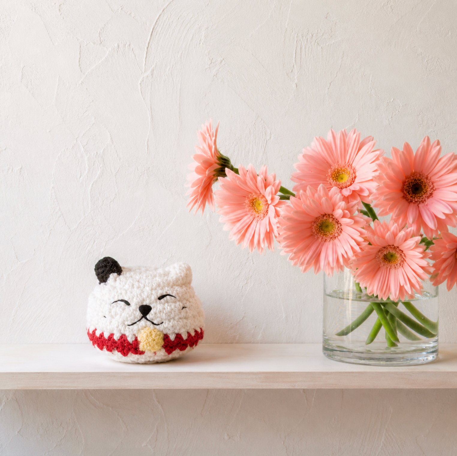Chunkle & Puff white woven lucky cat toy displayed on shelf beside pink flowers, soft plush texture and small decorative scale