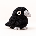 halloween cat toy. A black crocheted raven crocheted toy with a light gray beak, feet, and eye patch, photographed on a clean white background.