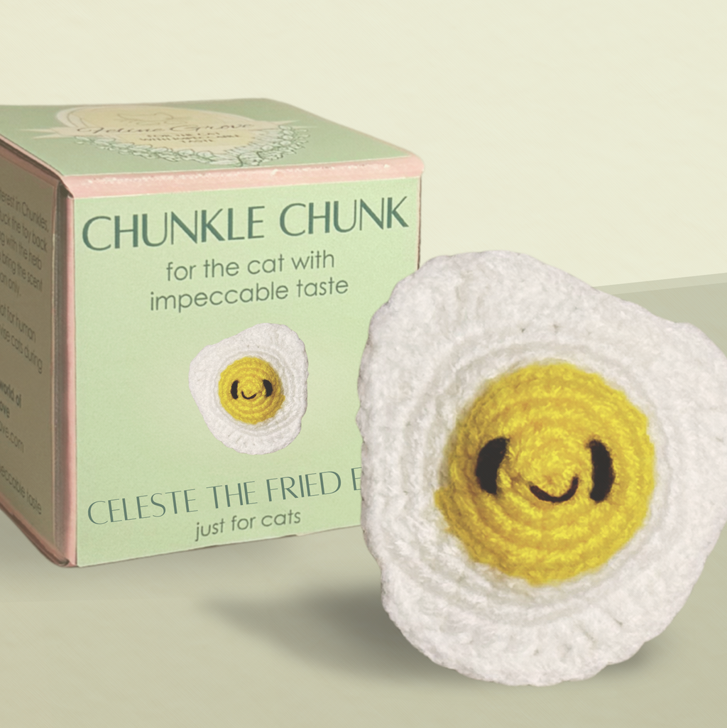 Celeste the Fried Egg Chunkle and Puff cat toy with packaging, woven egg design with textured white edges and yellow center, luxury cat toy for indoor cats infused with Miracle Nip botanical blend by Feline Grove including silvervine and valerian
