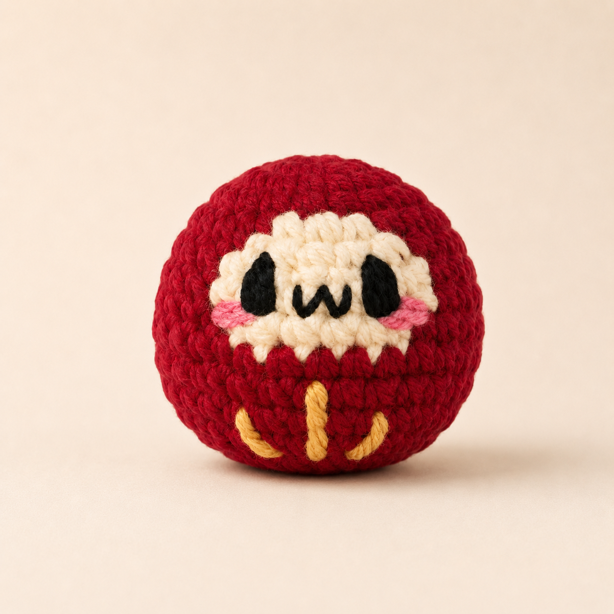 Japanese Cat Toy Daruma Doll in Red. Red daruma doll cat toy named Ichigo on a white background, showing its rounded shape, embroidered face, plush texture, and yellow stitched details.