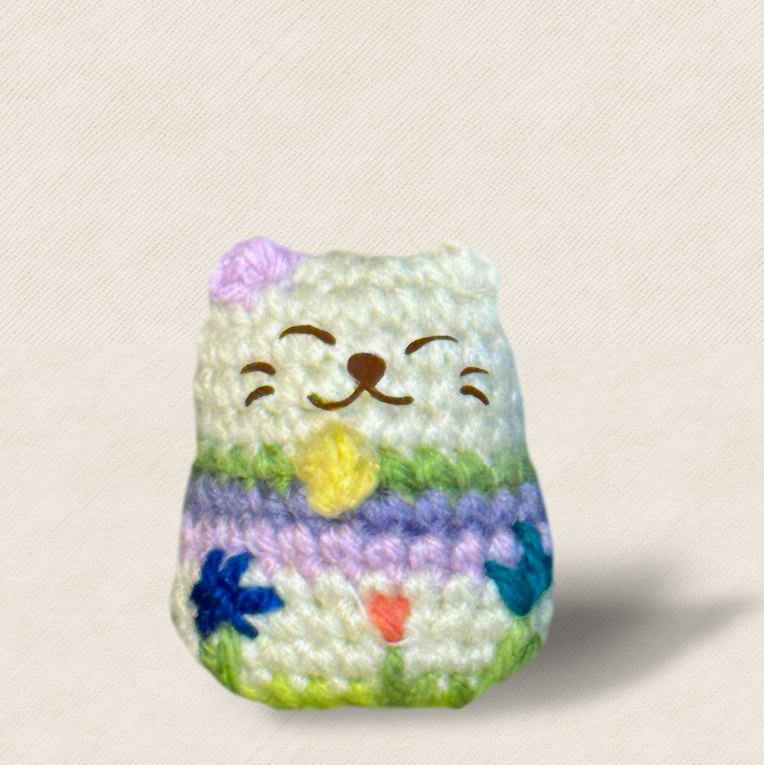 Close-up of woven luckycat toy with pastel stripes and embroidered face, soft textured surface and compact rounded shape designed for batting and carrying, artisan Chunkle & Puff cat toy infused with Miracle Nip catnip alternative