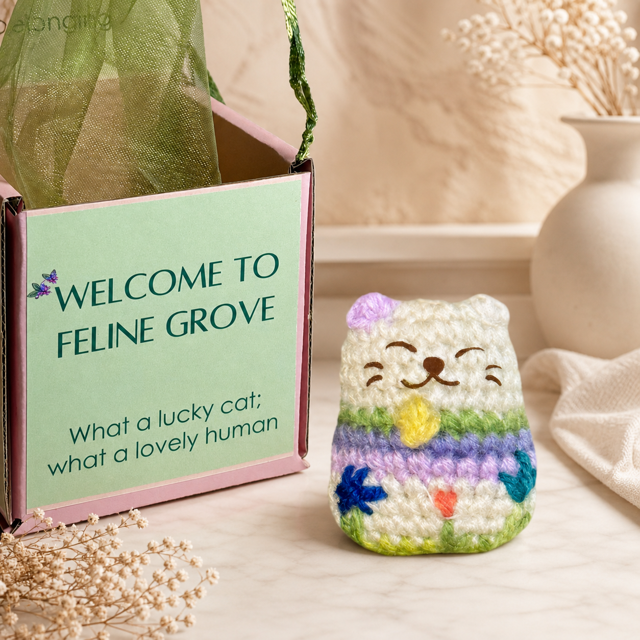 Woven lucky cat toy beside Feline Grove gift box with green organza bag, soft pastel stripes and embroidered face, compact rounded shape for batting and carrying, artisan Chunkle & Puff cat toy infused with Miracle Nip gourmet catnip alternative botanical blend