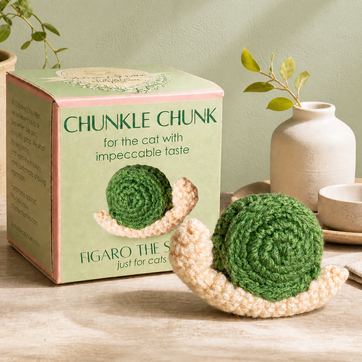 Artisan woven snail cat toy with green spiral shell resting in cupped hands, soft textured surface and small palm-sized scale, lightweight form for batting and carrying, Chunkle & Puff toy infused with Miracle Nip