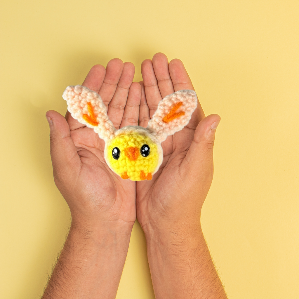 Wally the Chick small cat toy resting in open hands to show scale; compact, palm-sized design with soft woven texture, yellow body, and long cream ears.